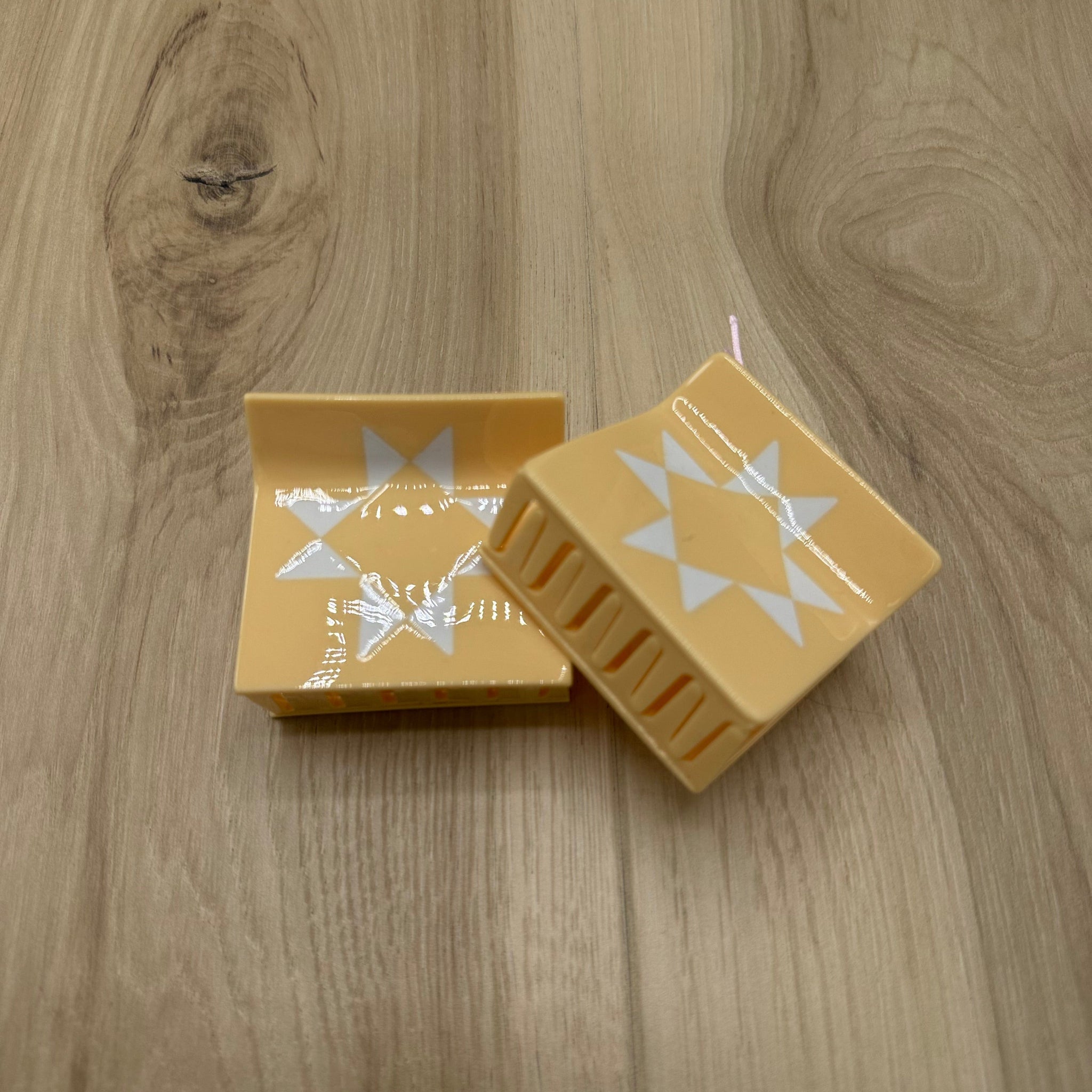 Two butter-yellow hair claw clips with star designs on a wooden surface