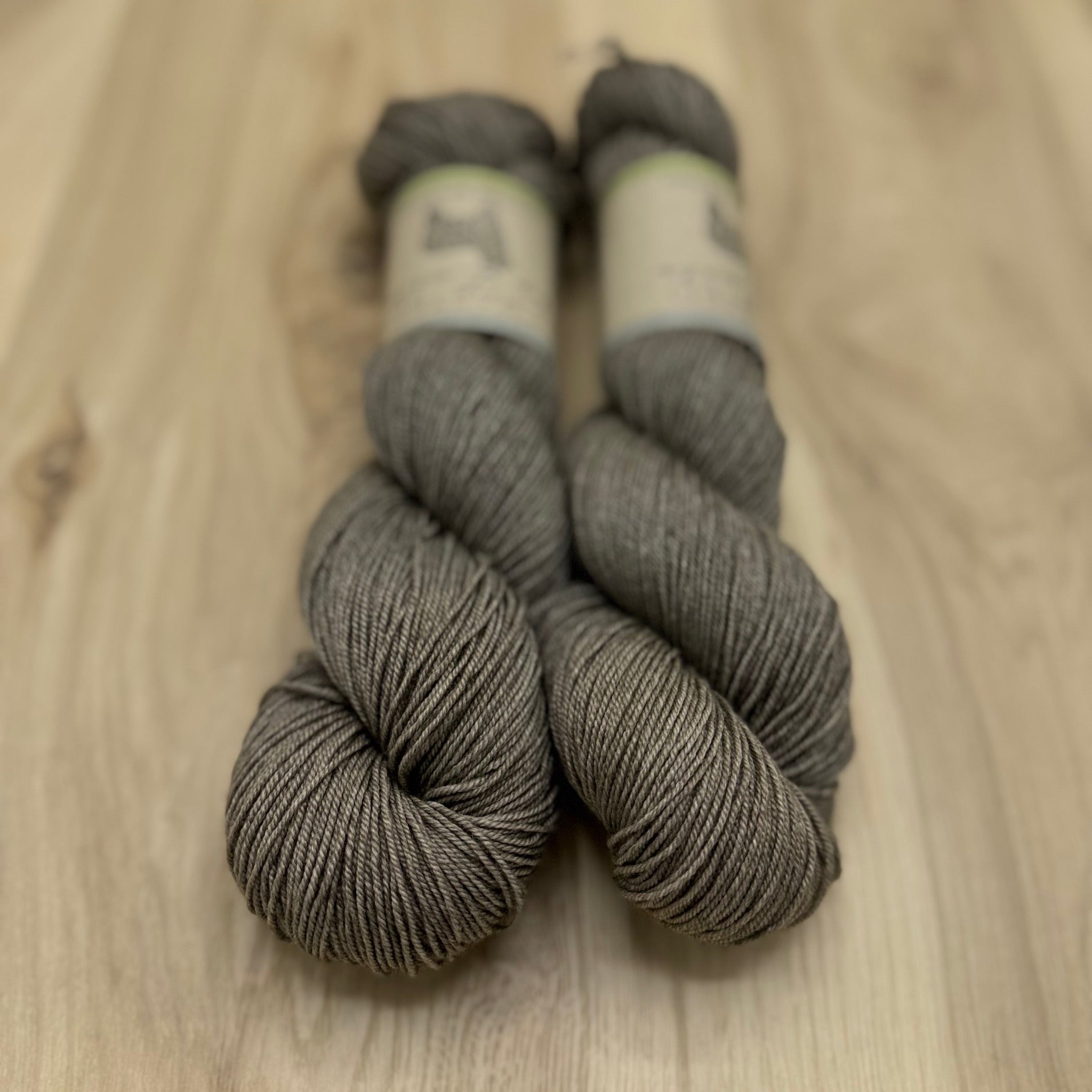 Two skeins of light cool brown yarn on a wooden surface