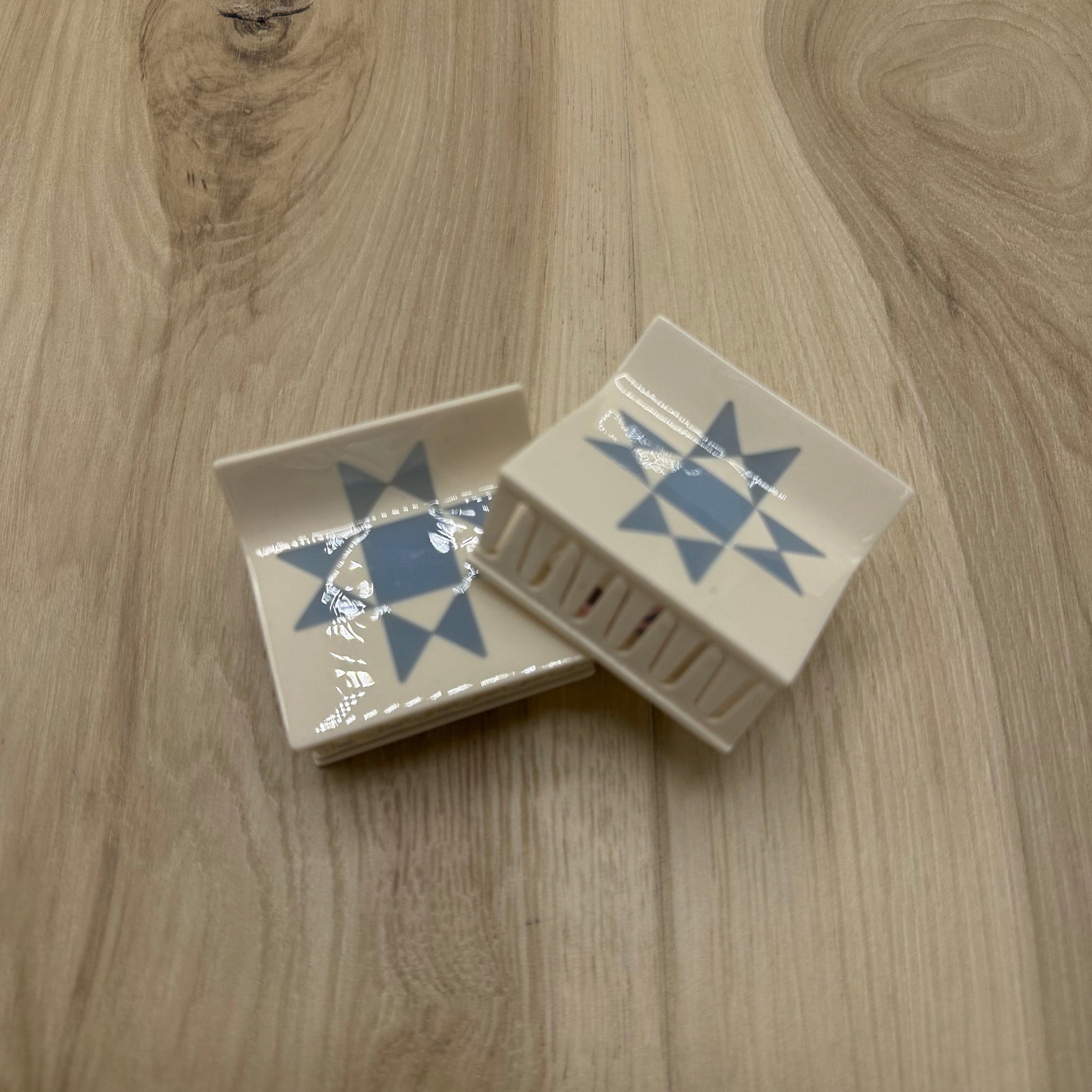 Two ivory colored hair claw-clips with blue  star patterns on a wooden surface