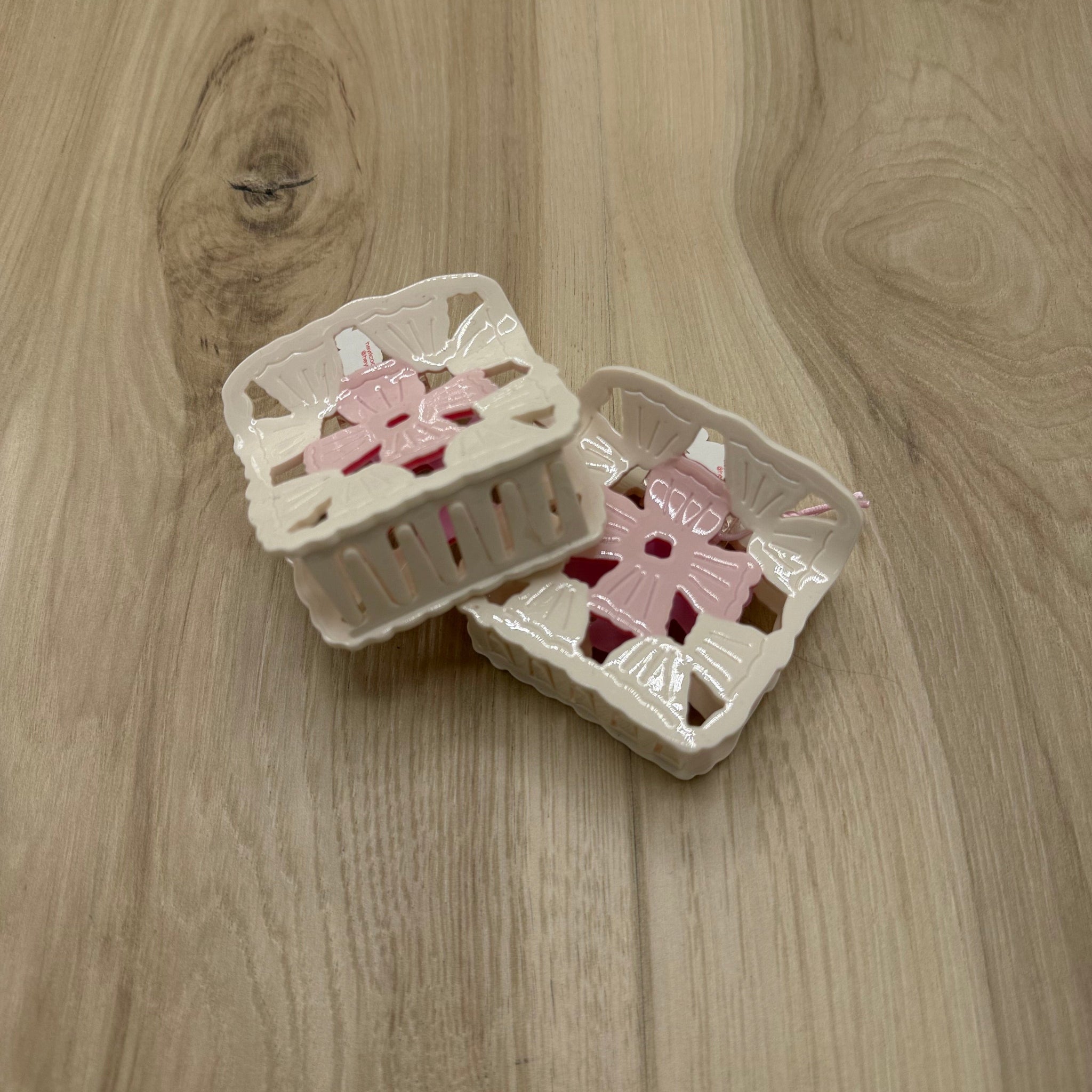 Two white and pink granny square design hair claw-clips on a wooden surface