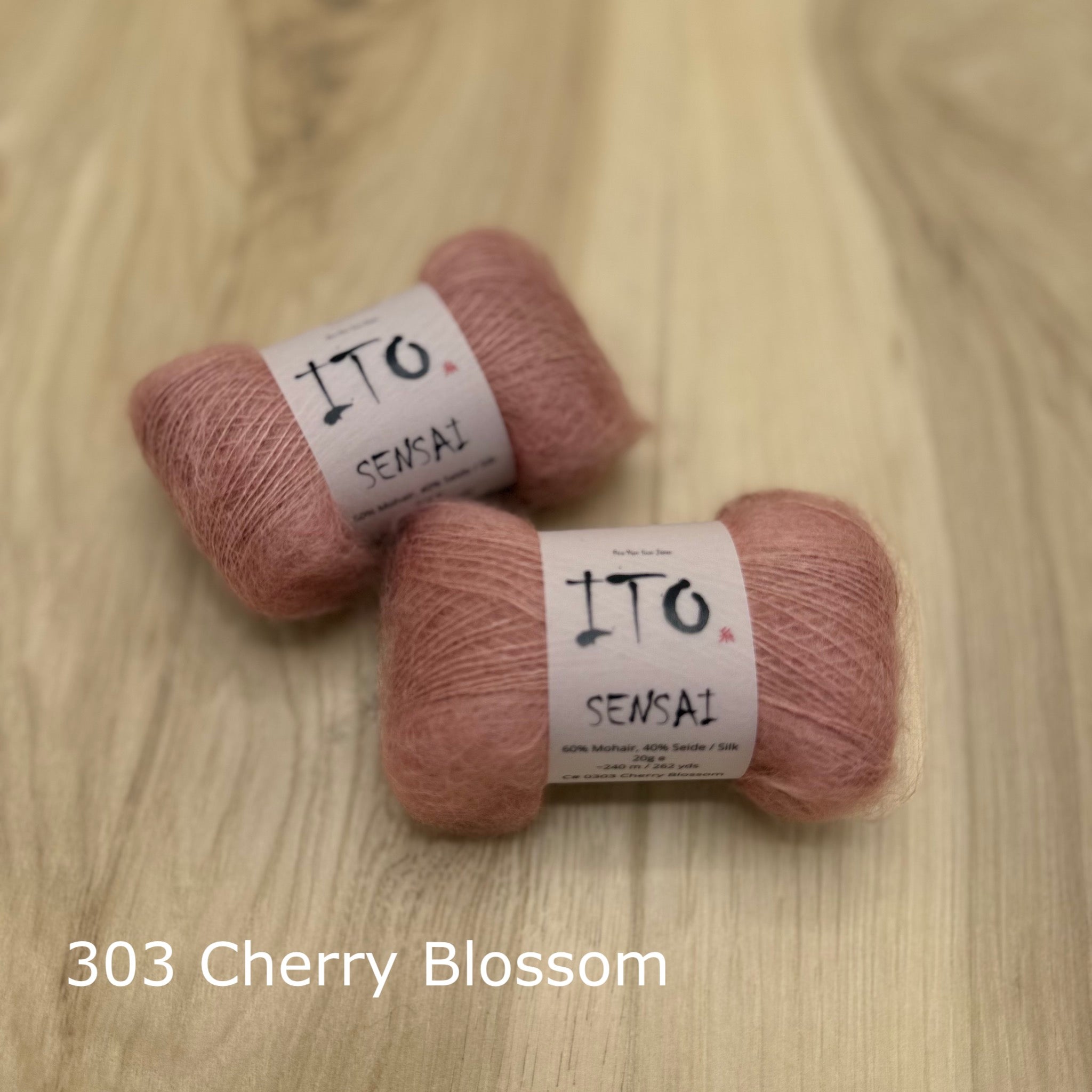 Two skeins of cherry blossom pink yarn labeled 'ITO Sensai' on a wooden surface.