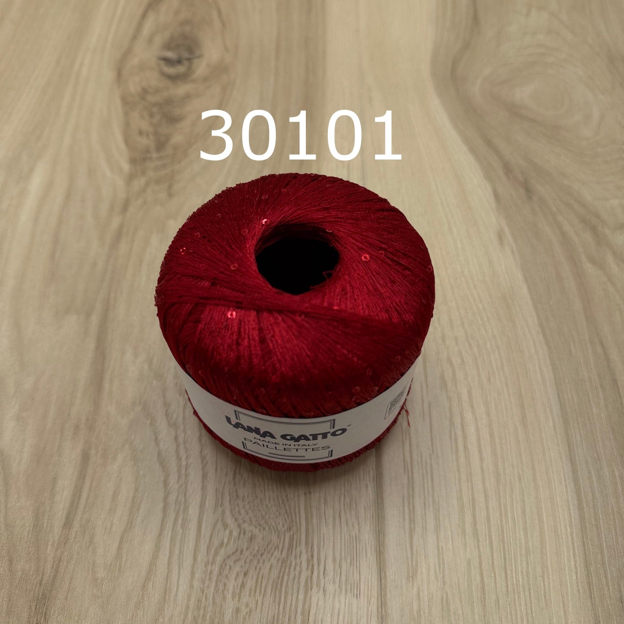 Red yarn ball with sequins  on a wooden surface
