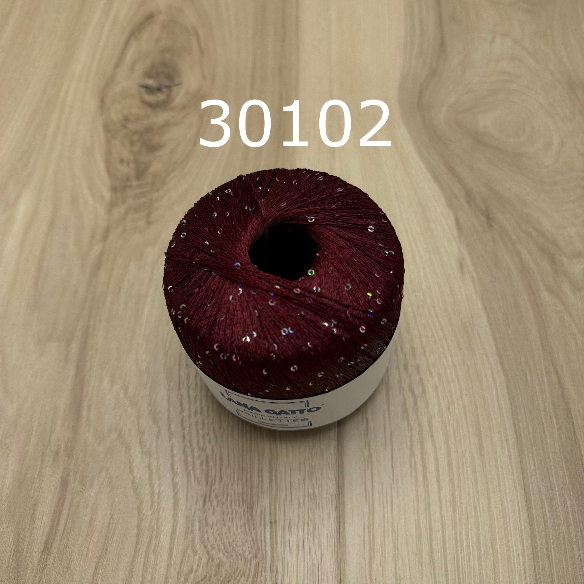 Maroon yarn ball with sequins on a wooden surface