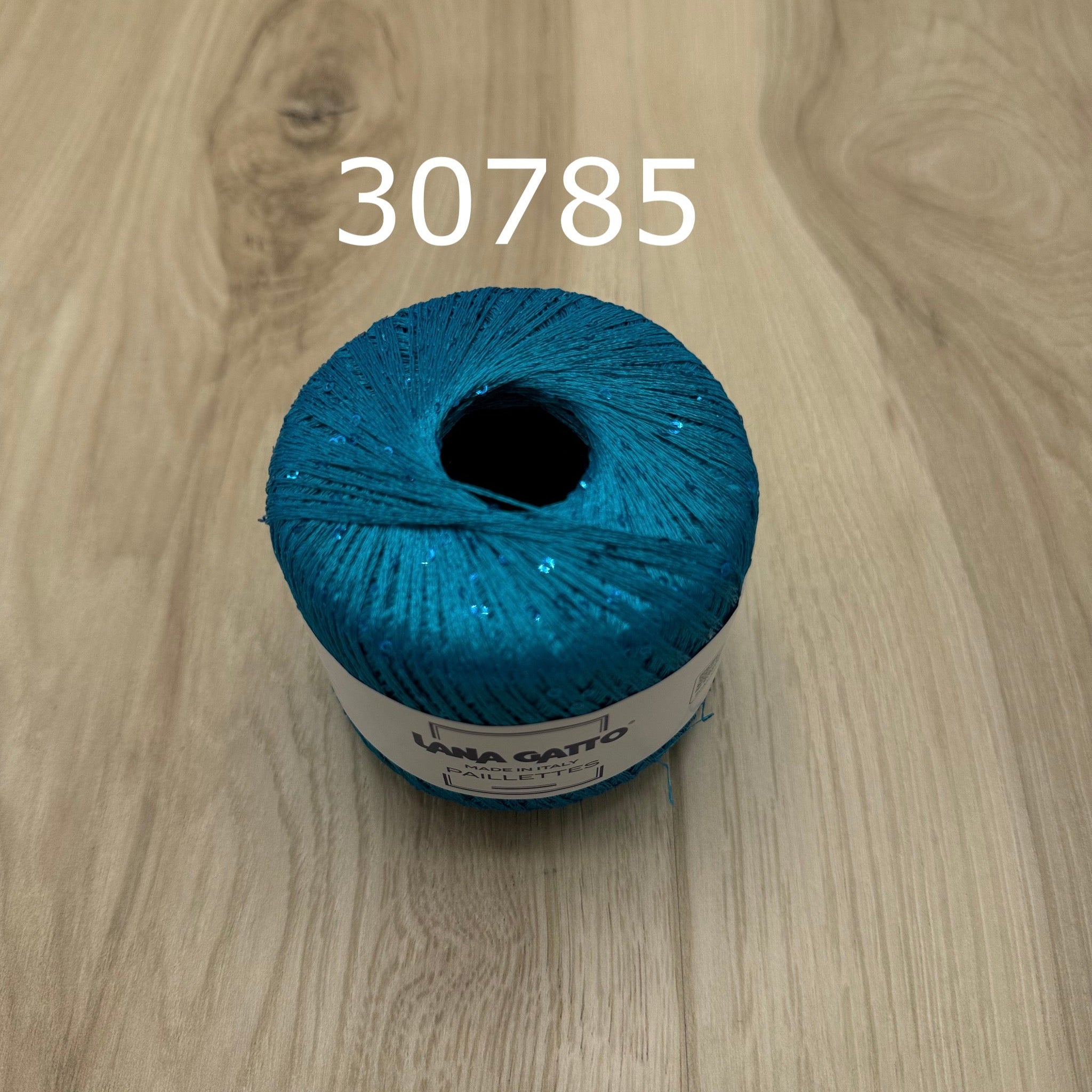 Turquoise blue yarn ball with sequins on a wooden surface 
