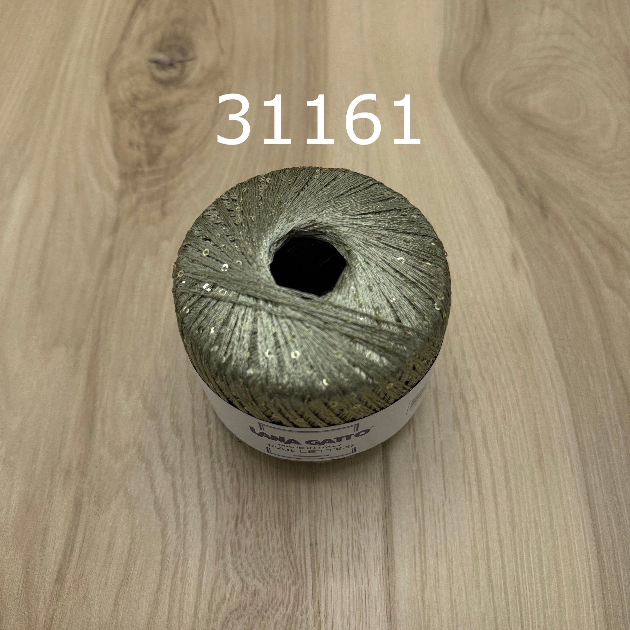 Sage green ball of yarn with sequins on a wooden surface