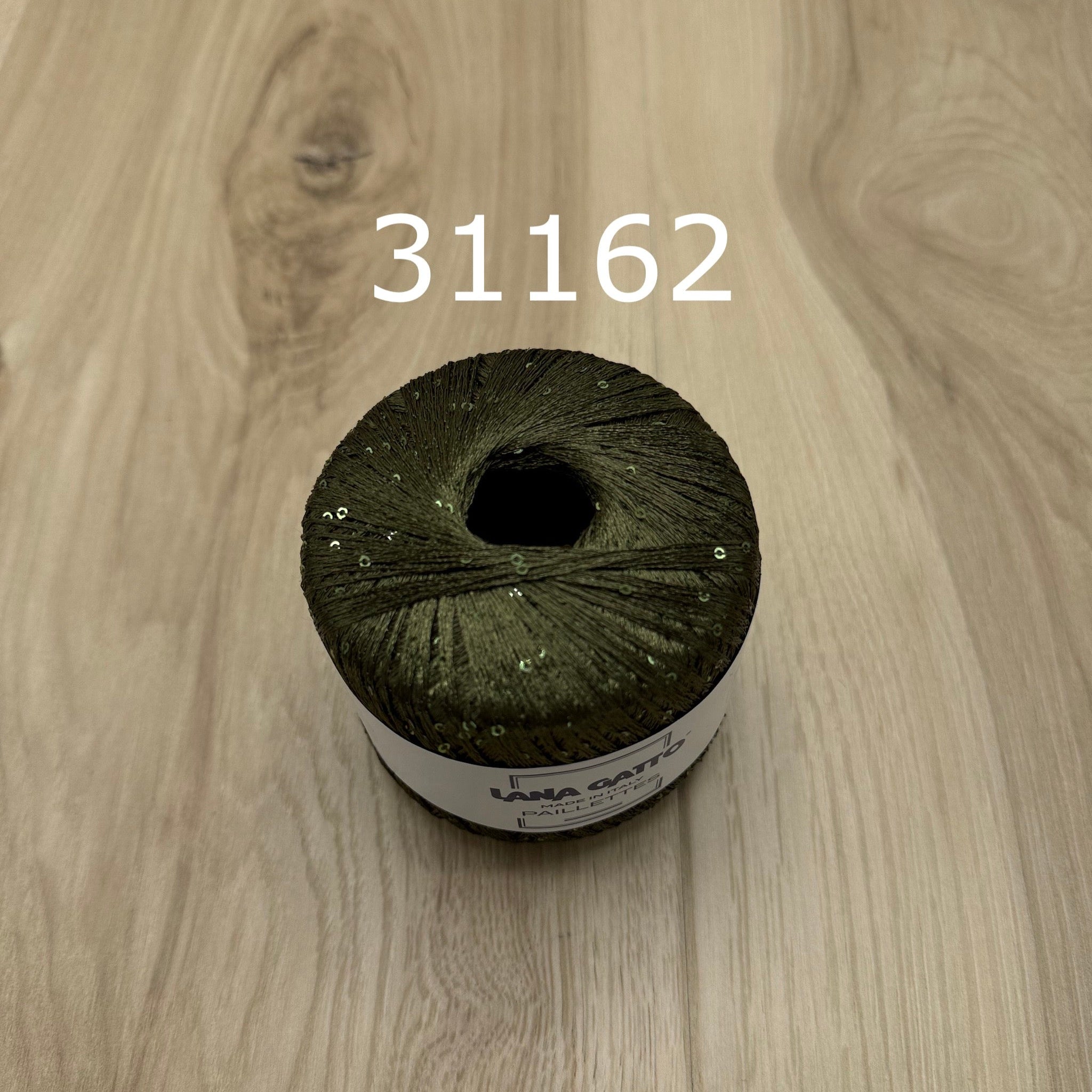 Olive green ball of yarn with sequins on a wooden surface