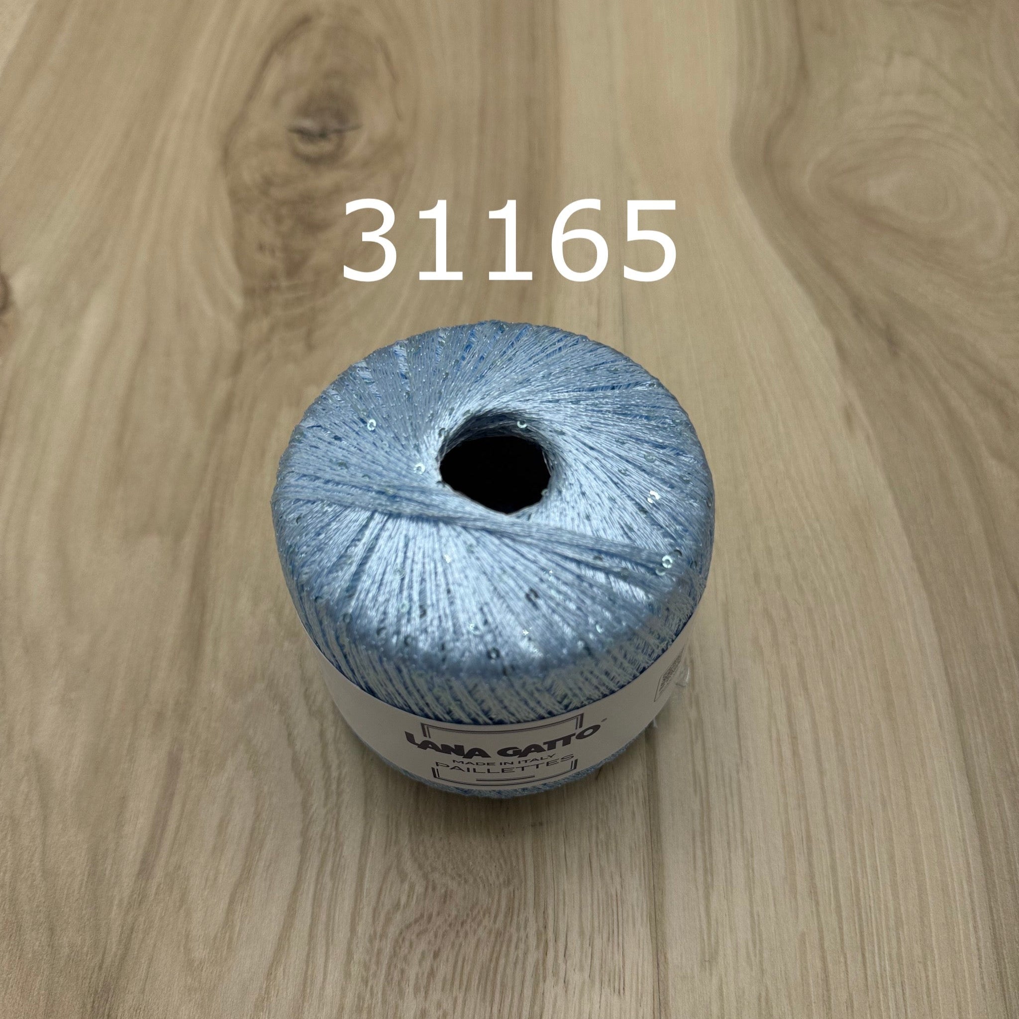 Light blue ball of yarn with sequins  on a wooden surface