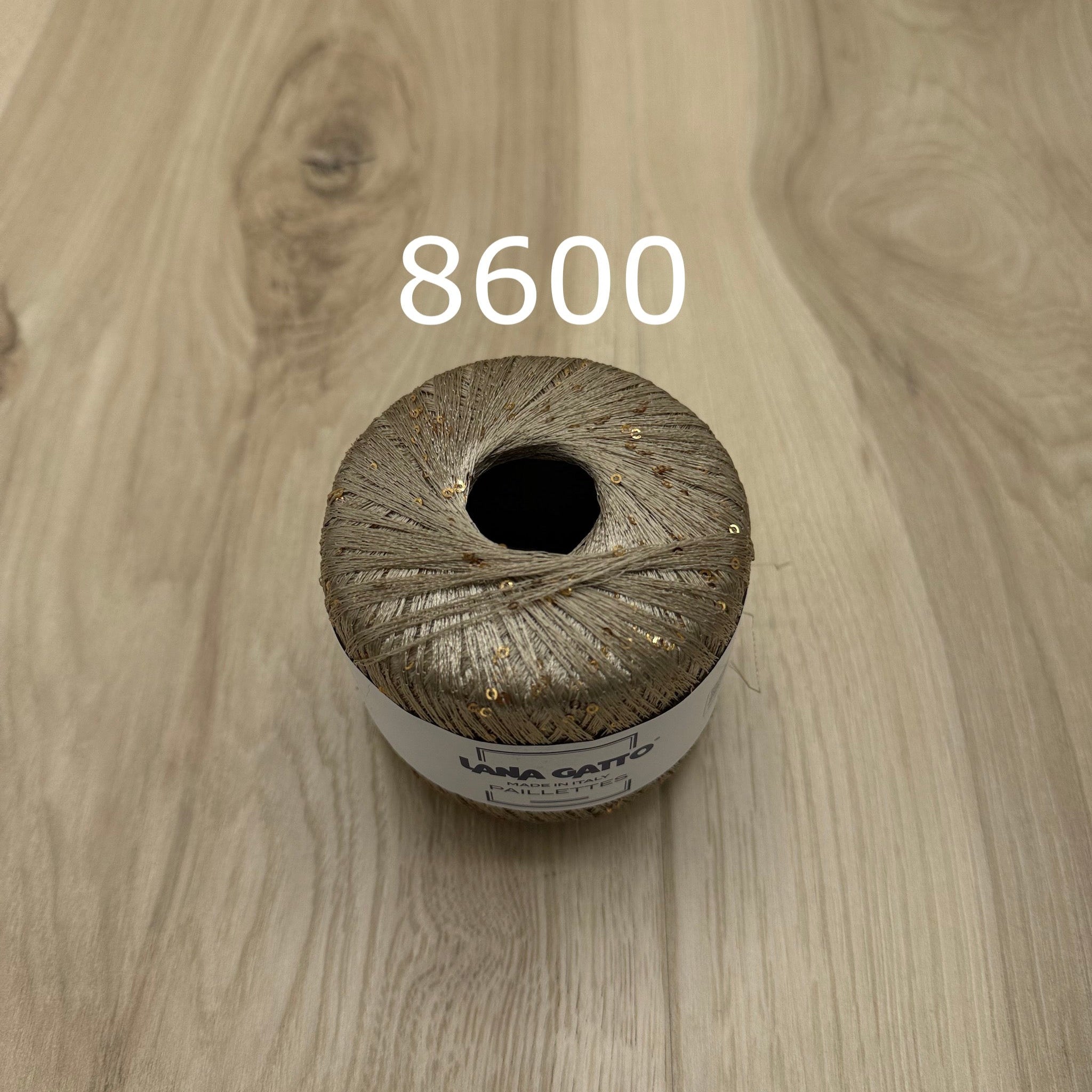 Tan ball of yarn with sequins  on a wooden surface