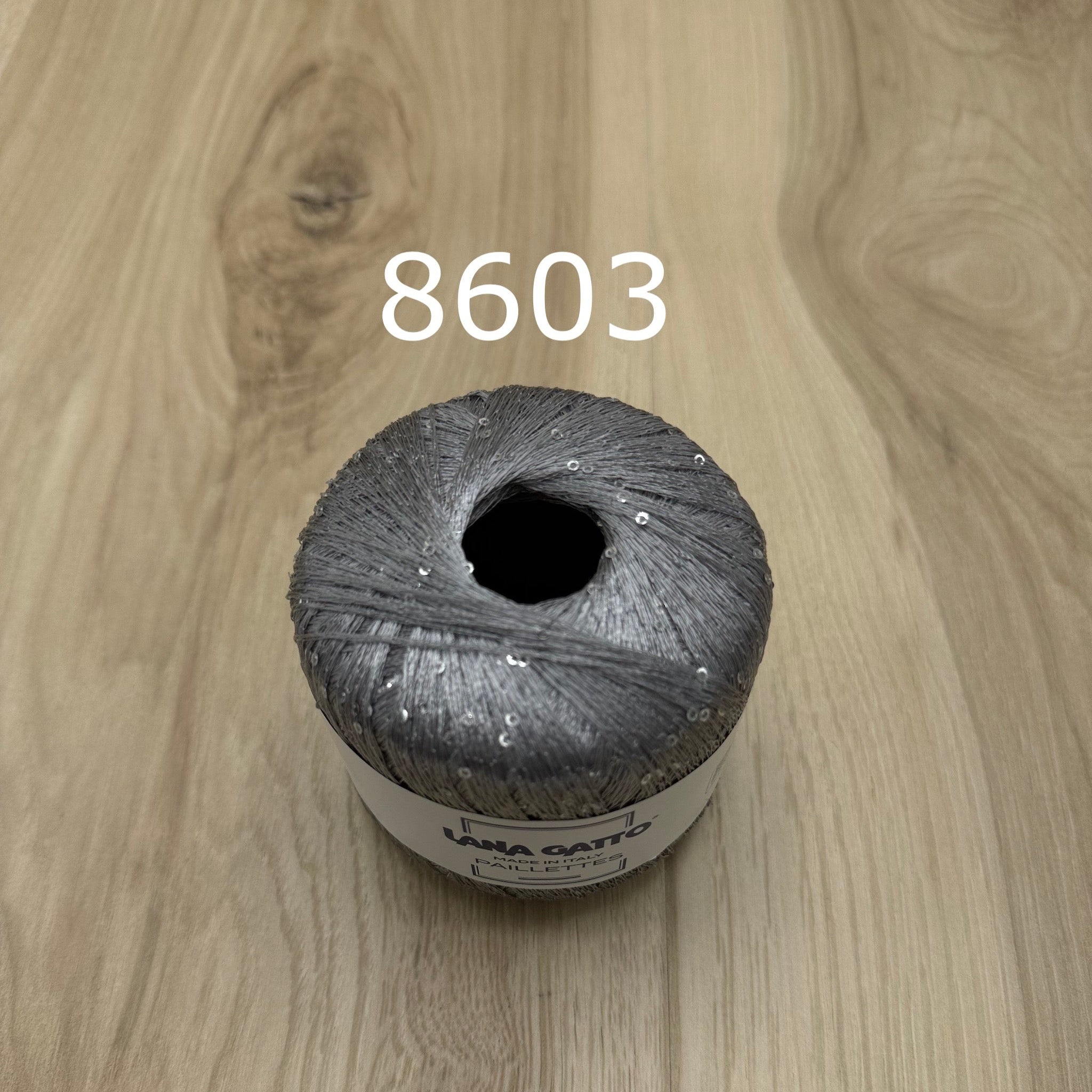 Silver ball of yarn with sequins on a wooden surface,