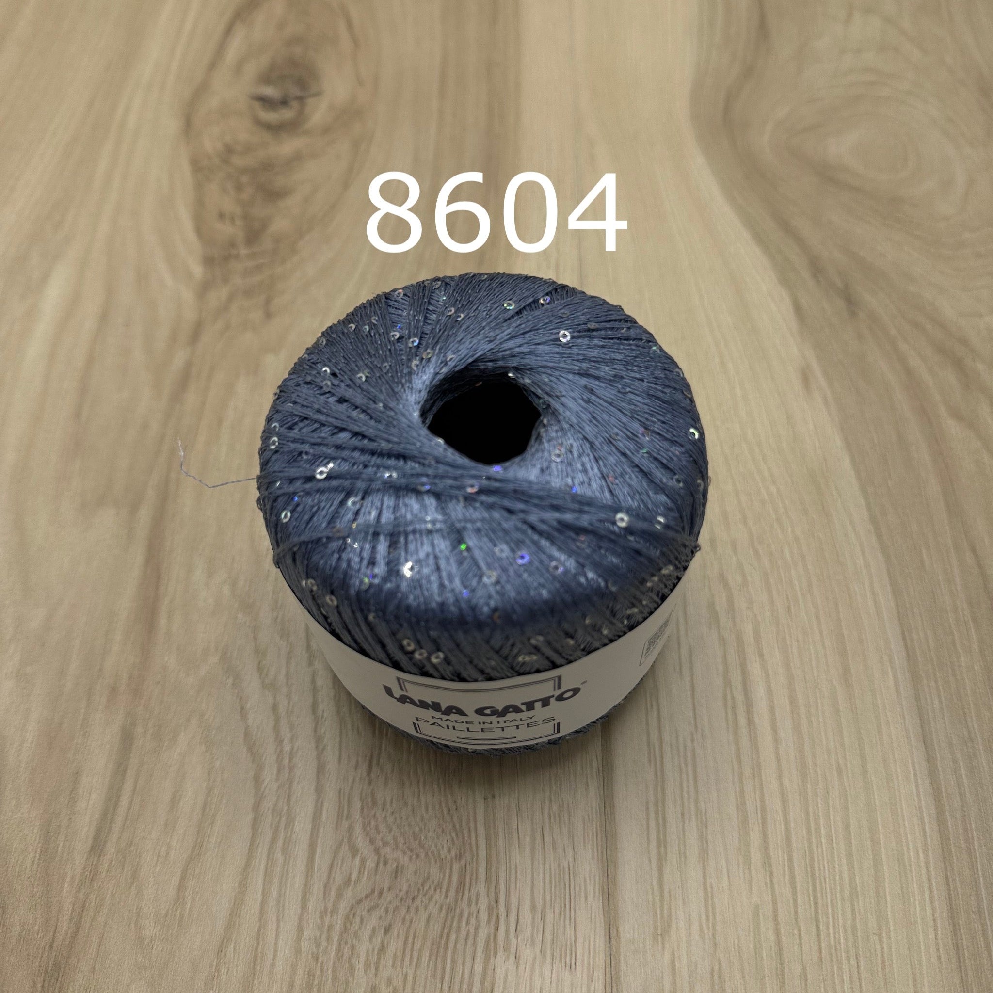 Blue-gray ball of yarn with sequins on a wooden surface