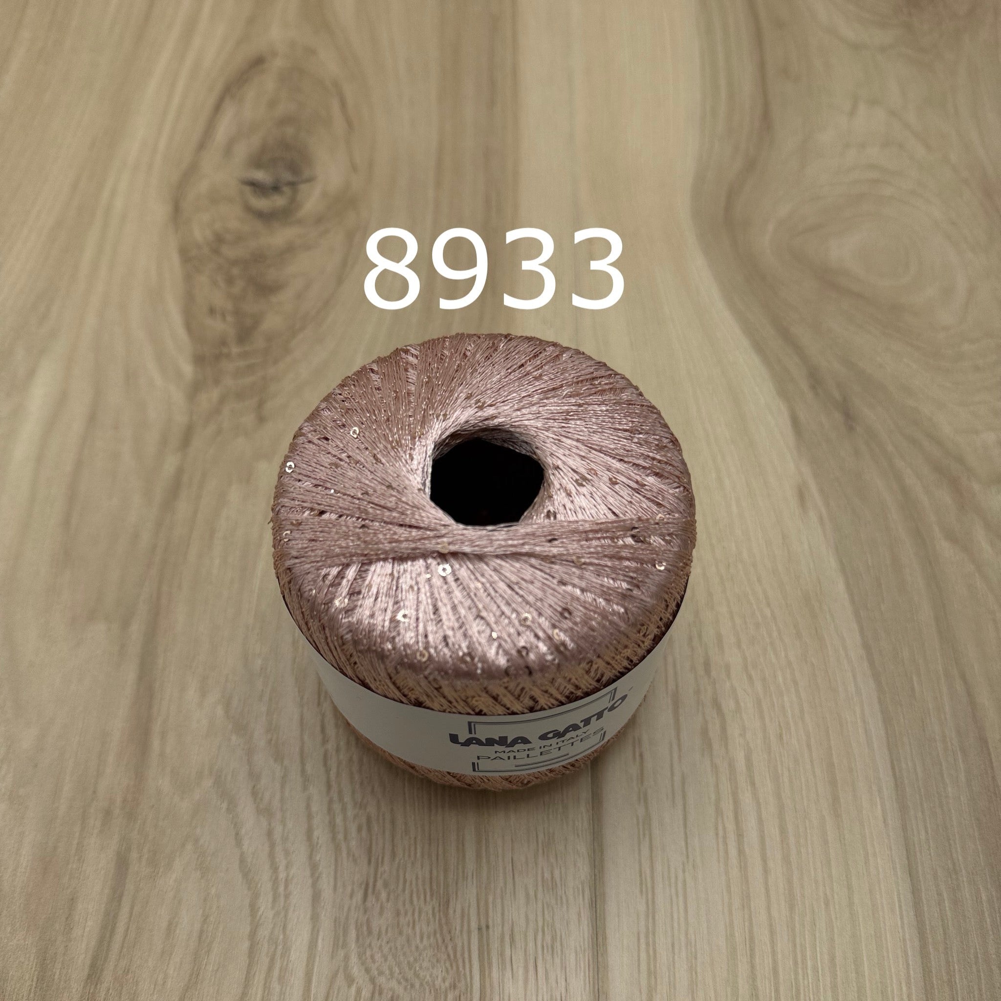 Pink ball of yarn with sequins on a wooden surface