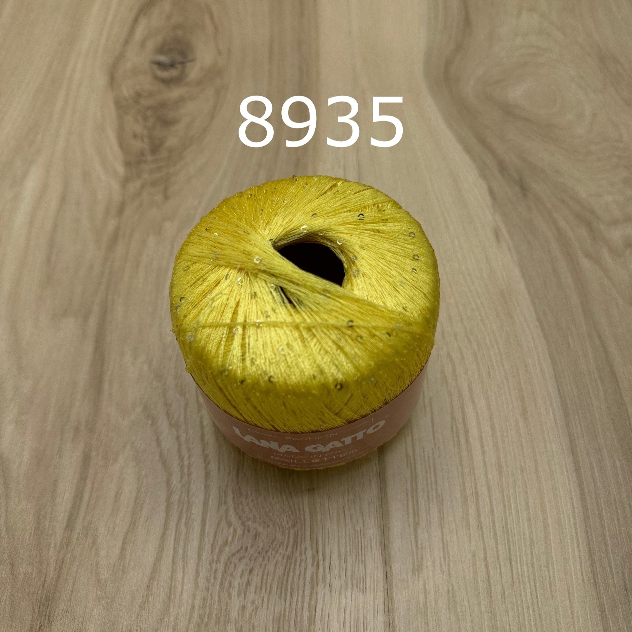 Yellow ball of yarn with sequins on a wooden surface