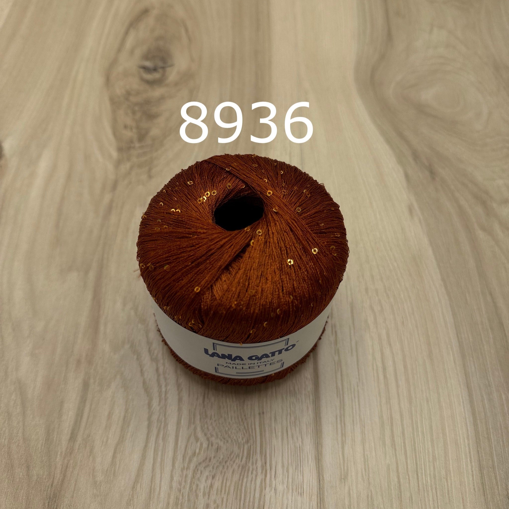 Rusty orange yarn ball with sequins on a wooden surface