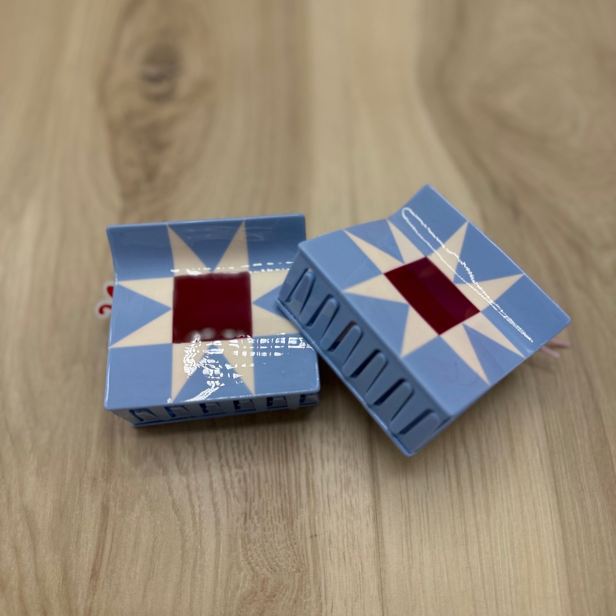 Two blue, red, and white quilt block hair claw clips  on a wooden surface