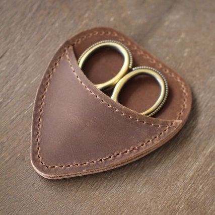 Brown leather case with gold scissors on a wooden surface