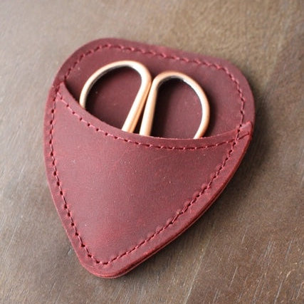 Heart-shaped leather case with a small gold tool on a wooden surface