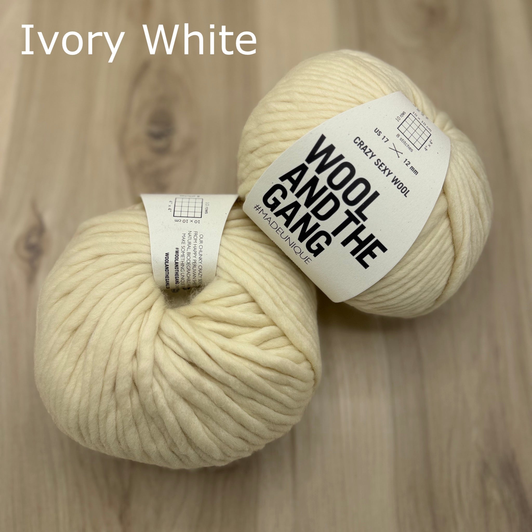 Two skeins of super-bulky ivory white yarn with 'Wool and the Gang' labels on a wooden surface.