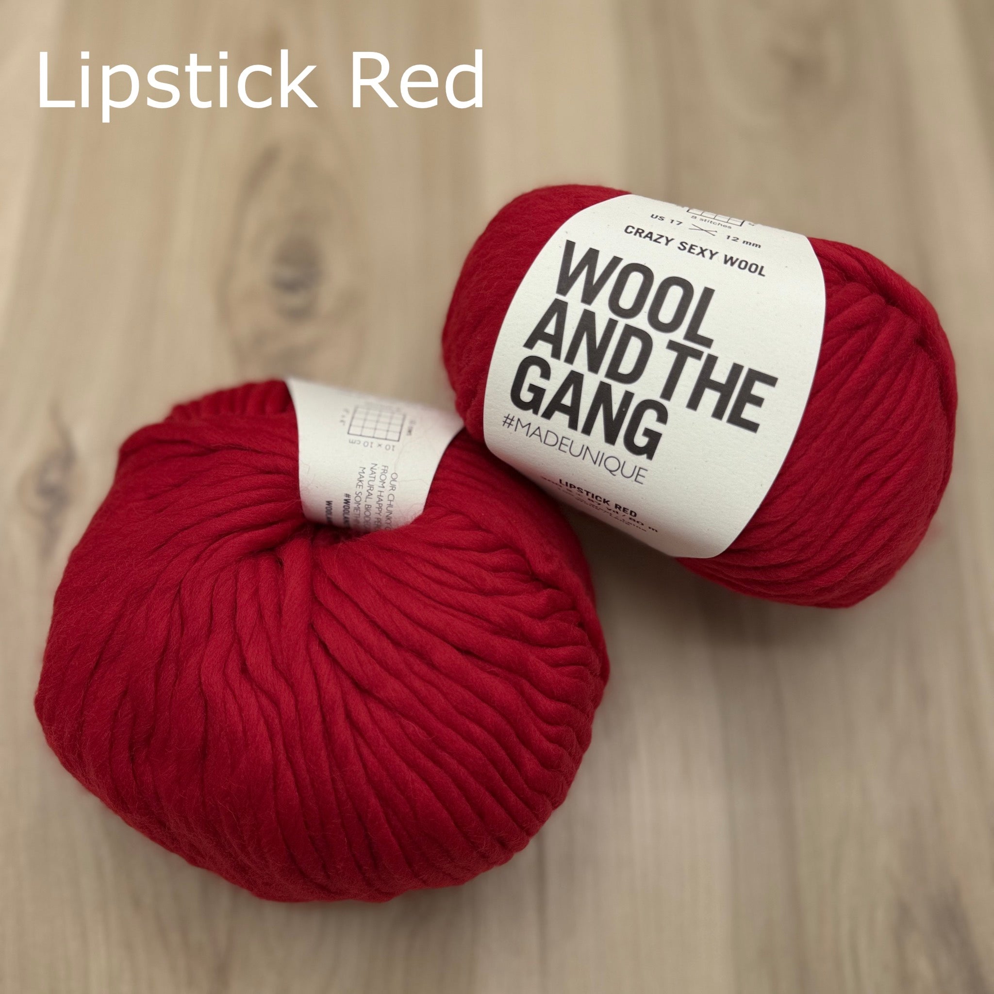 Two skeins of super-bulky red yarn with 'Wool and the Gang' label on a wooden surface