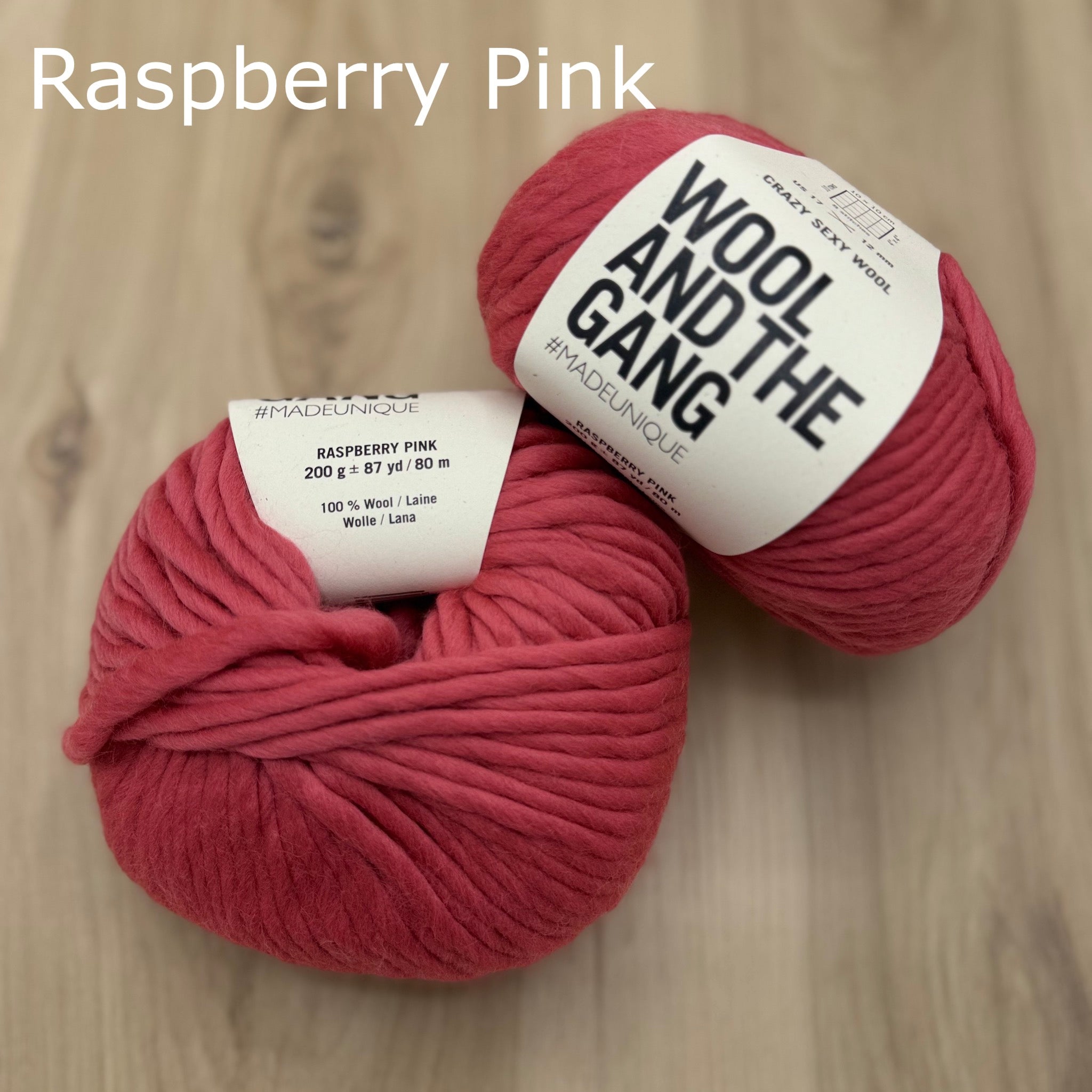 Two balls of super-bulky raspberry pink yarn with 'Wool and the Gang' label on a wooden surface