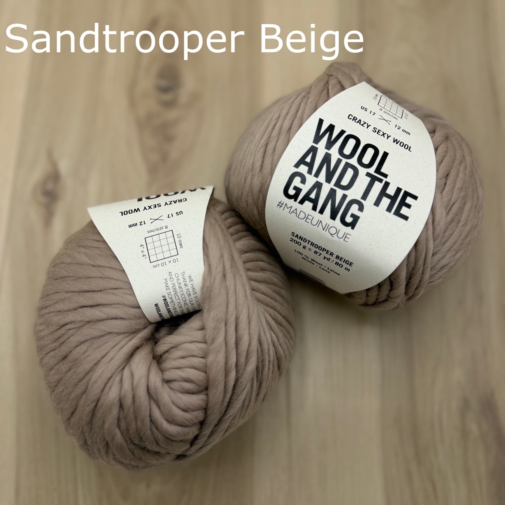 Two skeins of super-bulky light tan yarn labeled 'Wool and the Gang' on a wooden surface.