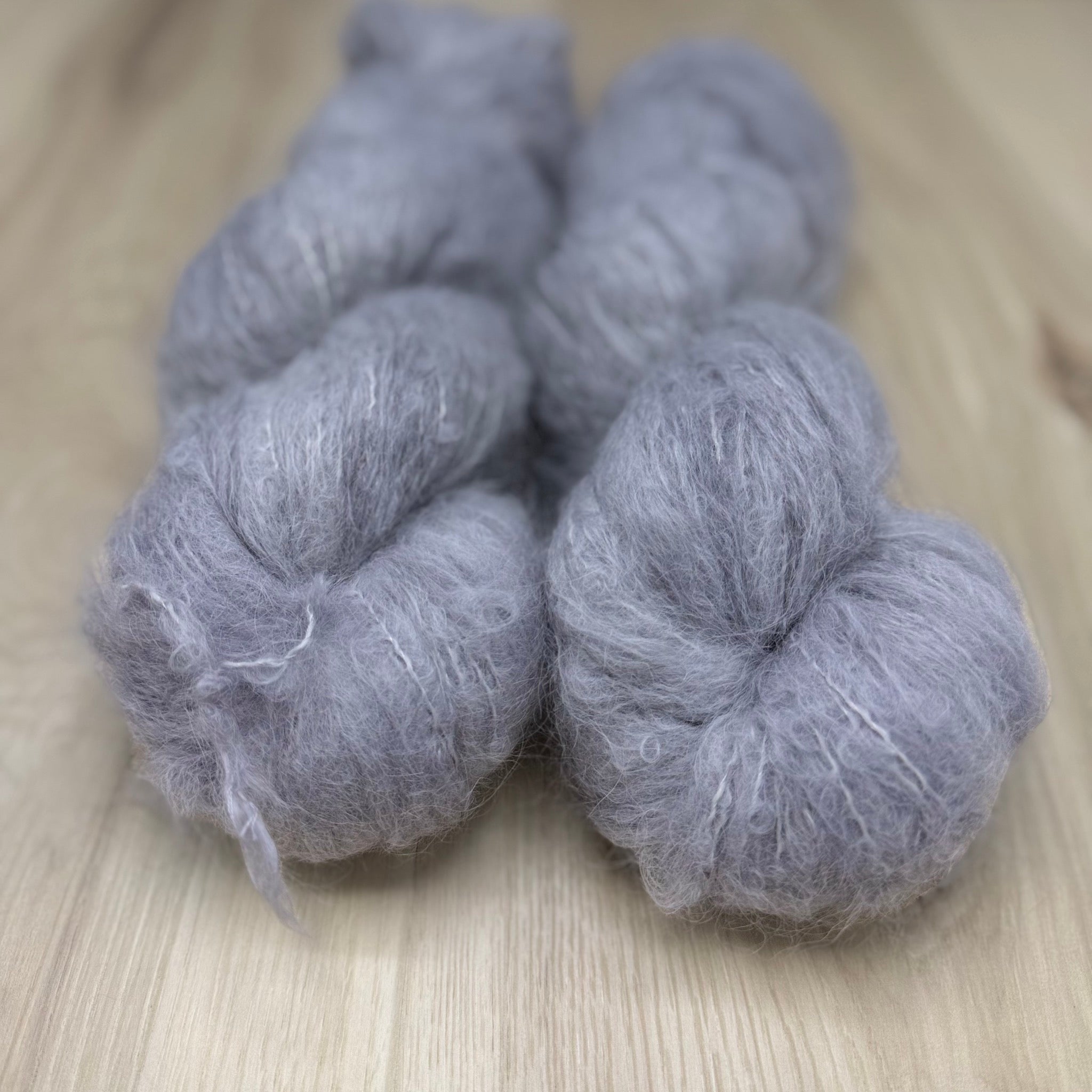 Two skeins of soft grey fuzzy yarn on a wooden surface