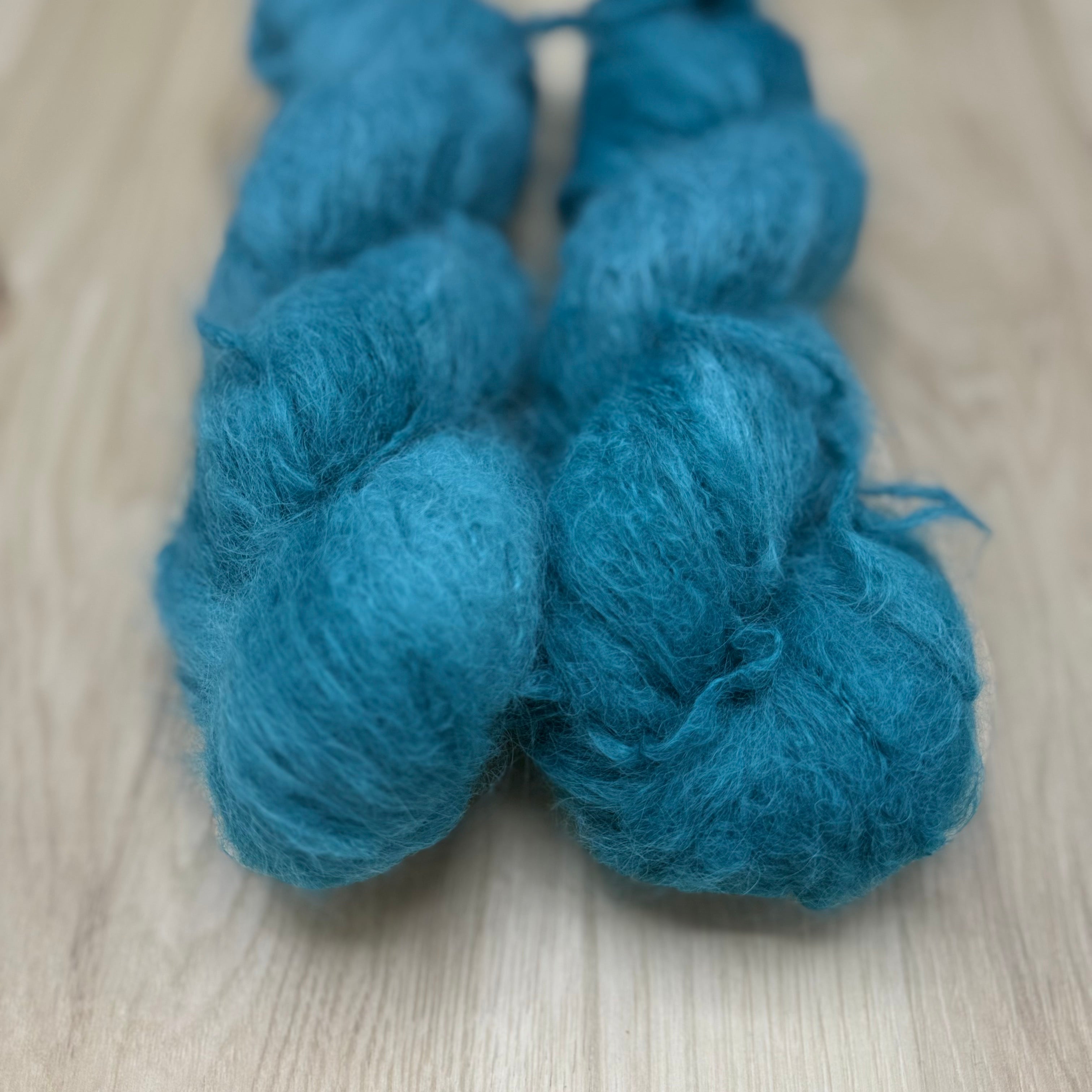 Two skeins of medium turquoise fuzzy yarn on a wooden surface