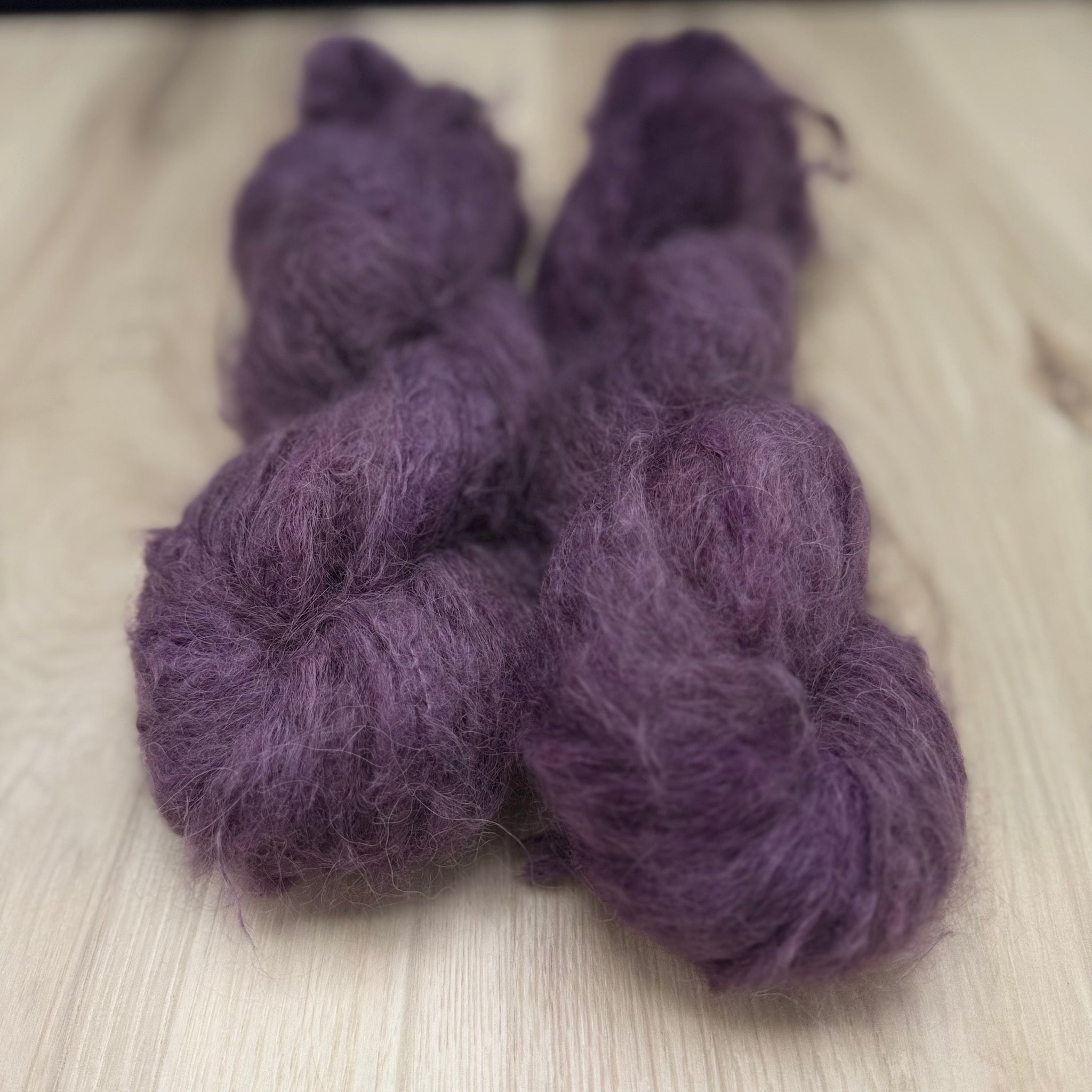 Two skeins of fuzzy purple yarn on a light wooden surface