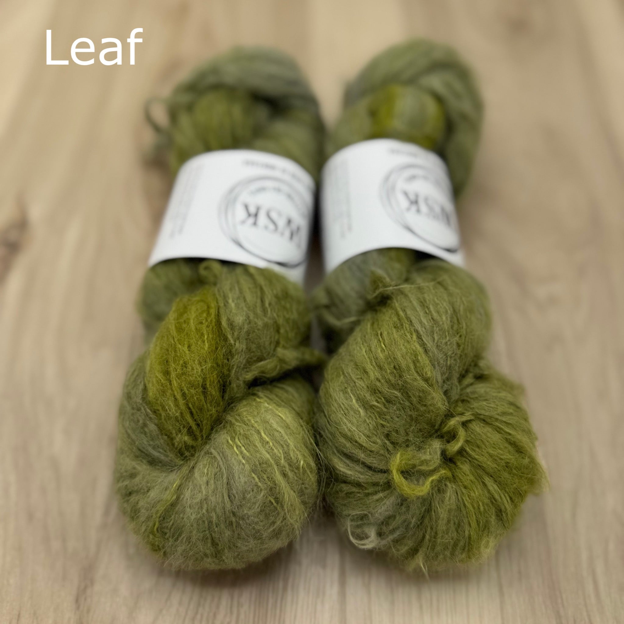Two skeins of leaf green fuzzy yarn on a wooden surface