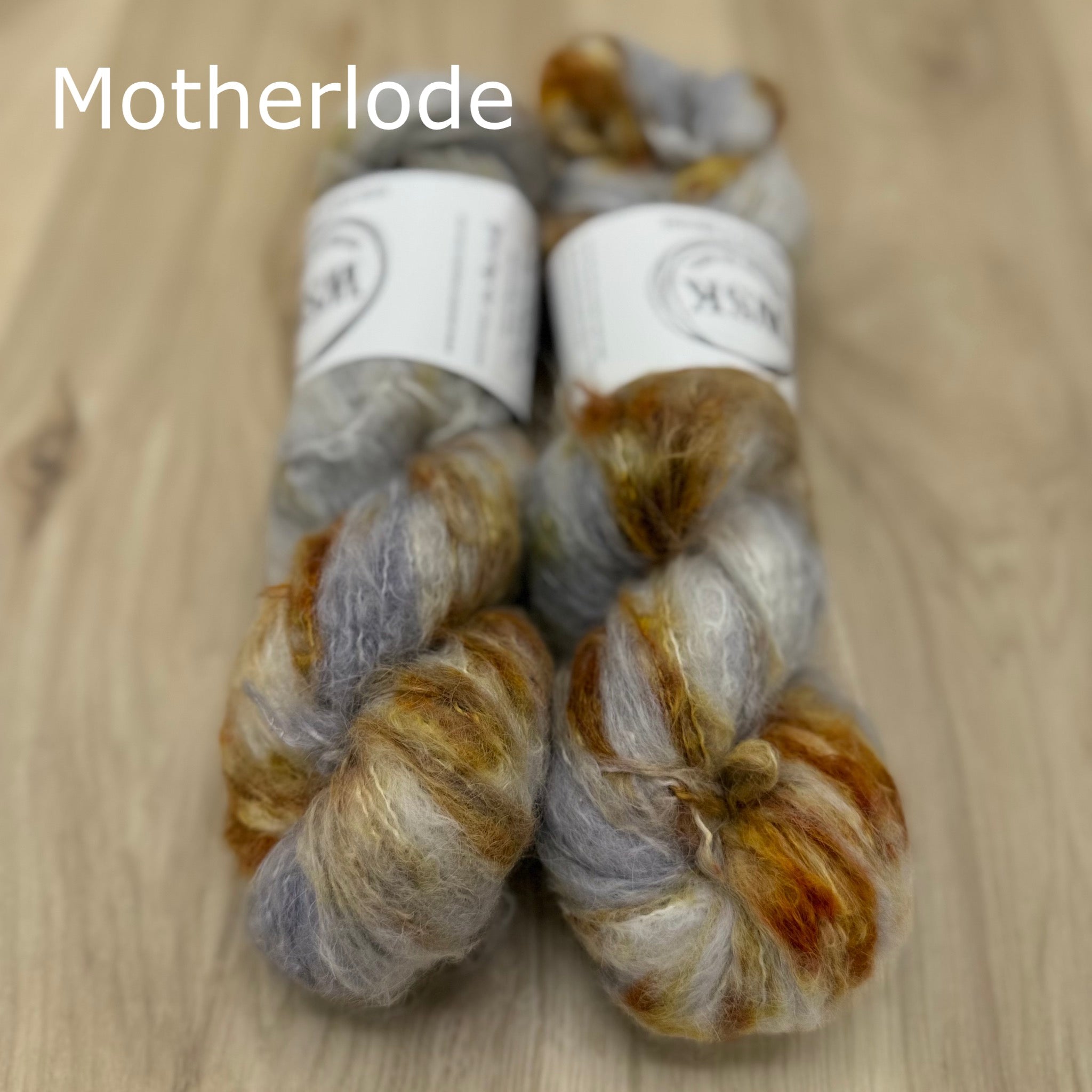 Two skeins of grey and gold fuzzy yarn on a wooden surface