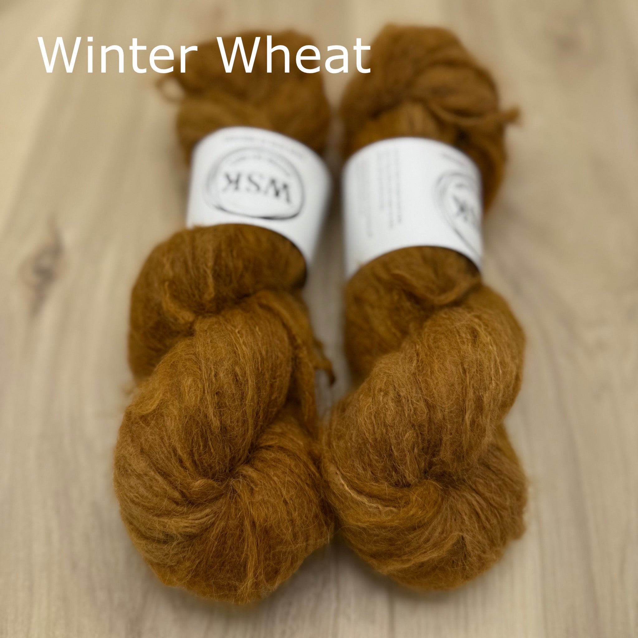 Two skeins of rusty brown fuzzy yarn labeled 'Winter Wheat' on a wooden surface.