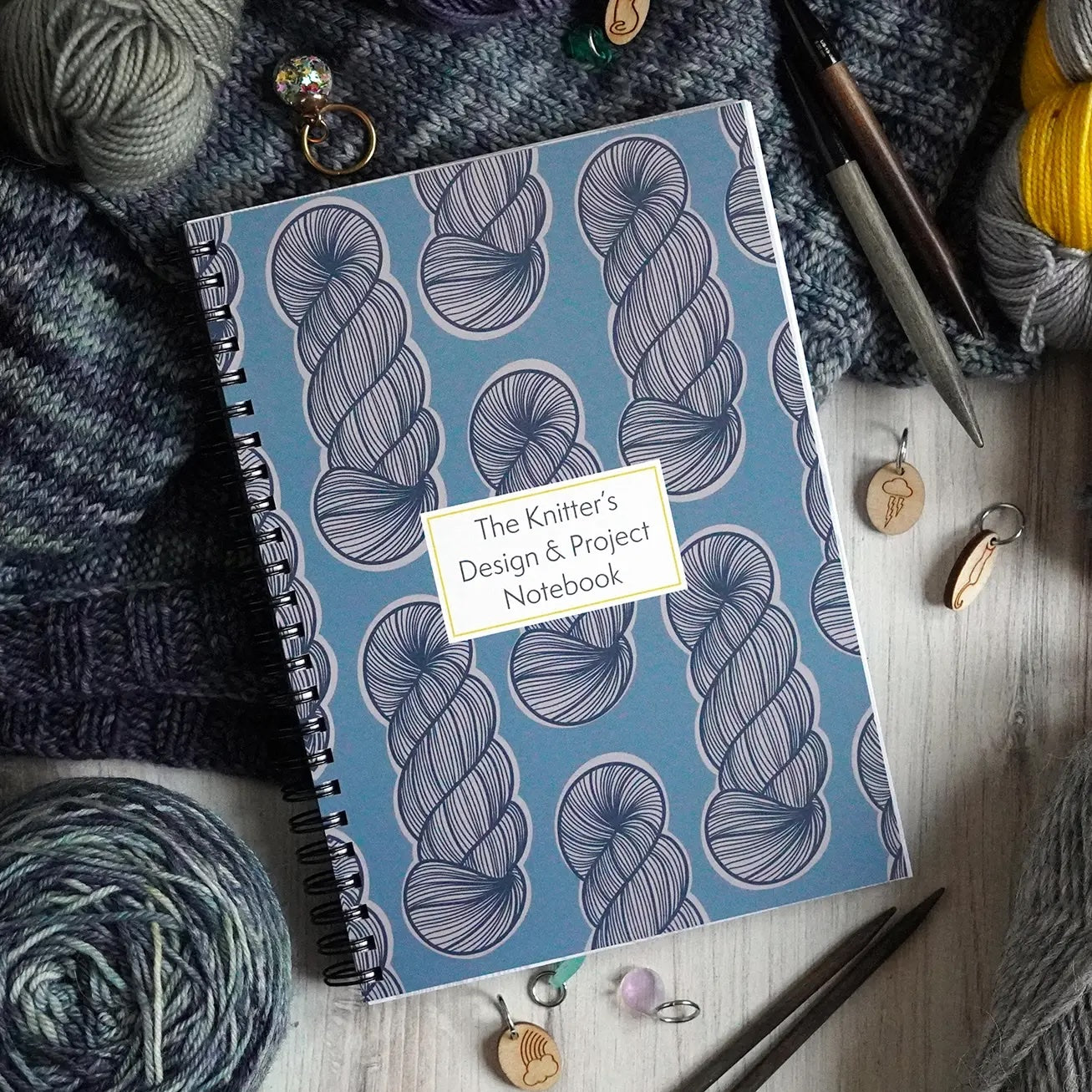 Knitter's design notebook with yarn and knitting tools on a wooden surface